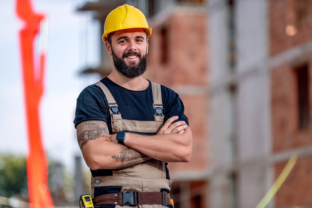 Arquitecto masculino exitoso en un sitio de construcción con los brazos cruzados, mirando a la cámara
. - Foto, imagen