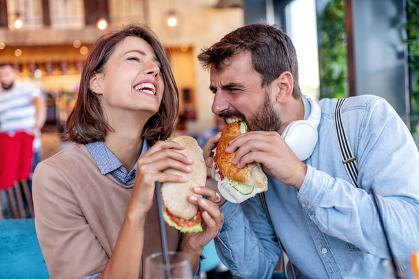 Молода весела пара п'є сік і їсть бутерброди в кафе. Люди, дата, любов і концепція способу життя
. - Фото, зображення