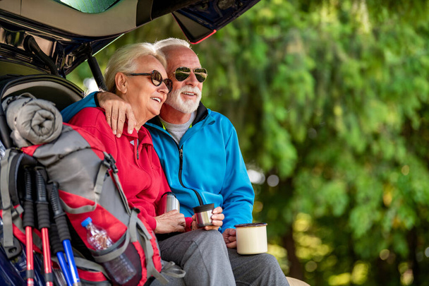 Senior couple sitting in car trunk and drink coffee while resting from hiking. - Fotoğraf, Görsel