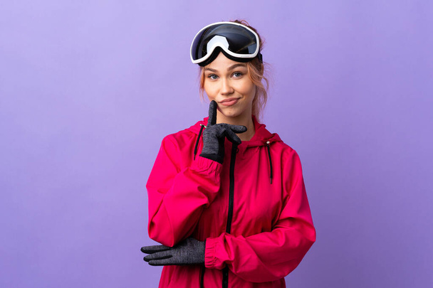 Лыжная девочка-подросток в очках для сноуборда на изолированном фиолетовом фоне и думает:
 - Фото, изображение