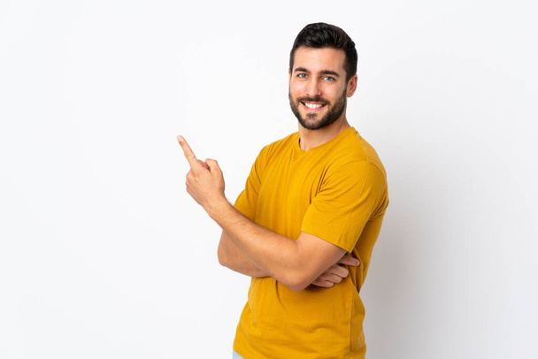 Fiatal jóképű férfi szakállal elszigetelt fehér háttér mutató ujját oldalra - Fotó, kép