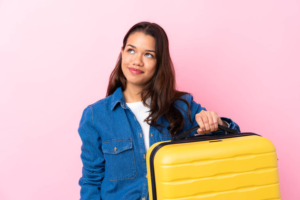 Traveler Colombian woman holding a suitcase over isolated pink background looking up while smiling - Valokuva, kuva