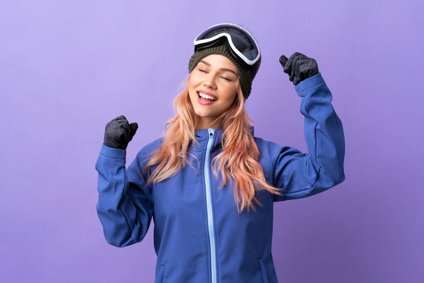 Skier teenager girl with snowboarding glasses over isolated purple background celebrating a victory - Photo, Image