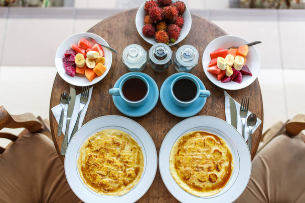 pancakes with banana, fruits and hot coffee on wooden table. - Foto, imagen