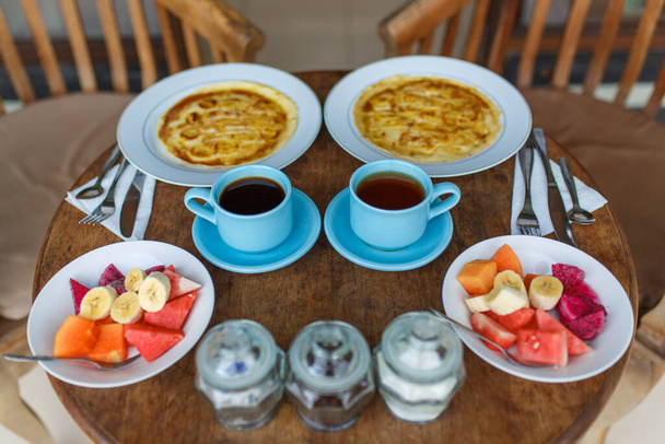 pancakes with banana, fruits and hot coffee on wooden table. - Fotoğraf, Görsel