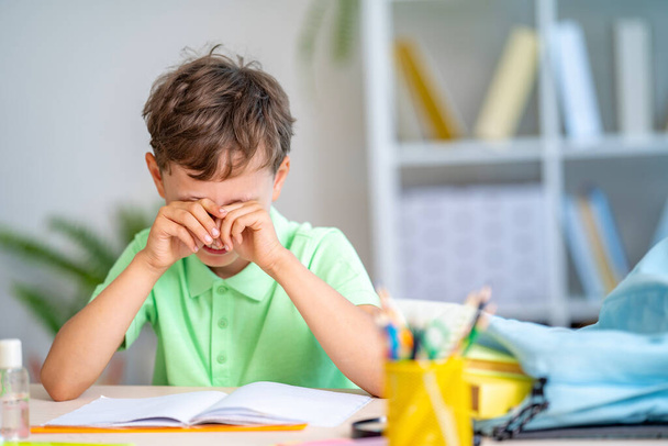 tired schoolboy cries, rubs his eyes, because he no longer wants to read or suffers from bullying. homework. boy rubs his eyes with fatigue, reading books and textbooks. problems with vision. - Foto, Bild