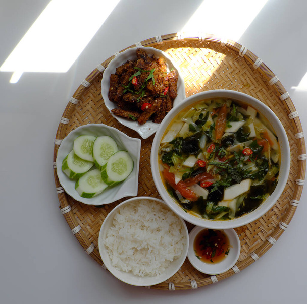 Bovenaanzicht dienblad van Vietnamese maaltijd voor lunch op witte achtergrond, vegetarisch zelfgemaakt eten met seitan gebakken met citronella, chili, kom groentesoep en rijstschotel, eenvoudige keuken uit plantaardige - Foto, afbeelding