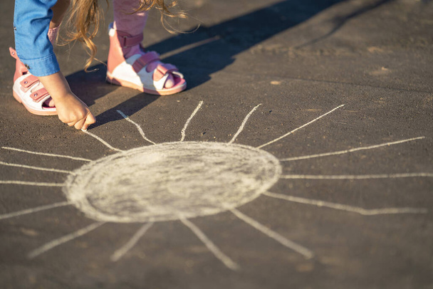 Close-up, a child draws with colored chalk on the asphalt. Children's day. A little girl draws the sun on the sidewalk with chalk. children walk in the fresh air. summer event. - Photo, image