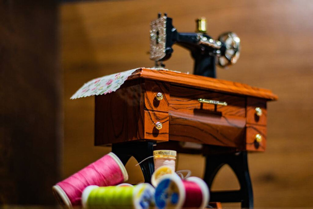 A toy sewing machine on the small wooden table with different threads and buttons next to it - Zdjęcie, obraz