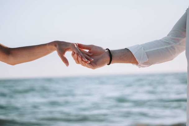 A selective focus shot of a couple holding hands with the sea on the background - Foto, imagen