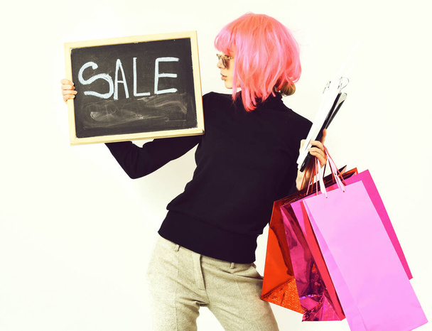 girl in wig holding package, hangers, board with sale inscription - Foto, immagini