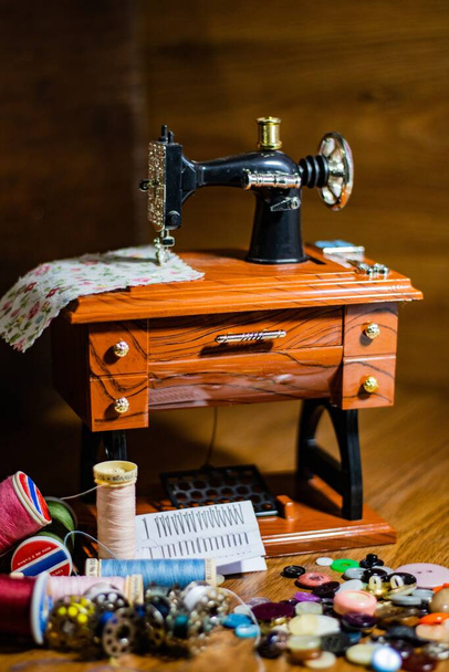 A toy sewing machine on the wooden table and colorful threads and buttons on the front of it - Valokuva, kuva