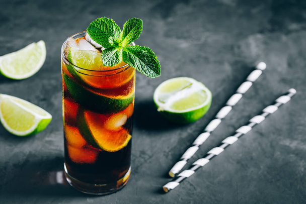 Rhum et Cola Cuba Libre boisson glacée cocktail avec citron vert et menthe sur fond sombre. - Photo, image