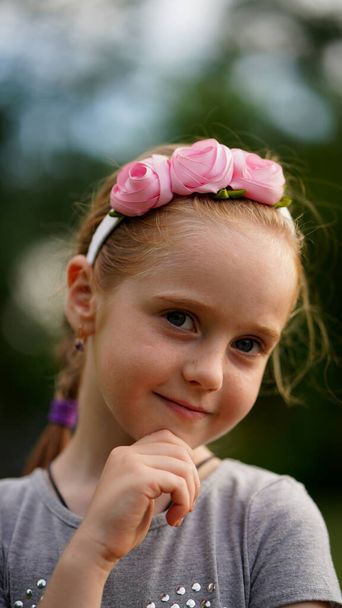 公園で夏に花と美しい髪の輪を持つきれいな女の子の肖像画。あごの近くに手を取り笑顔を保つ - 写真・画像