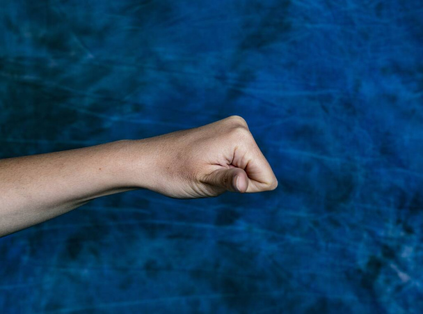 A horizontal shot of a fist with an open thumb pointing at the camera on a marbled blue background - Foto, Bild