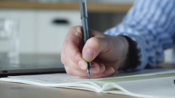 Primer plano de la mano de una mujer sosteniendo una pluma y escribiendo notas en un cuaderno sentado en casa
 - Metraje, vídeo