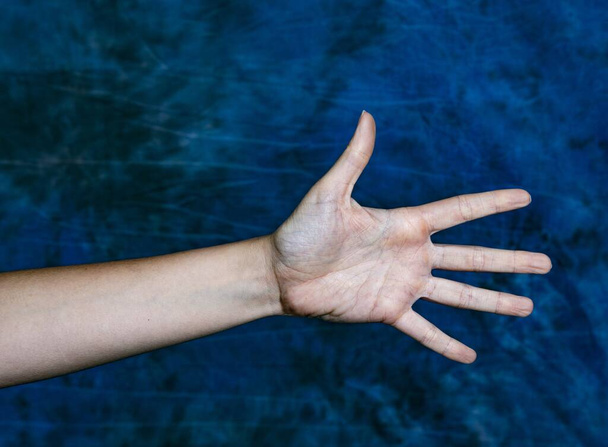 A horizontal closeup shot of a hand showing number five or an open palm on a marbled blue background - Foto, imagen