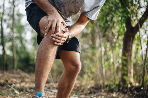 Спортивний молодий чоловік страждає від болю в коліні під час фізичних вправ у лісовому парку
 - Фото, зображення