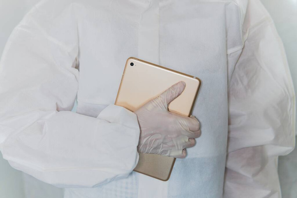 A healthcare worker holding a tablet wearing a protective bio hazard sterile suit and gloves to prevent infection by coronavirus - Photo, Image