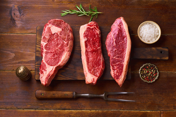  cutting board with ribeye, striploin and picanha fresh black angus prime raw beef steaks on wooden background, top view - Foto, immagini