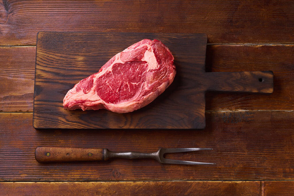 cutting board with black angus prime beef rib eye steak on wooden background, top view  - Fotoğraf, Görsel