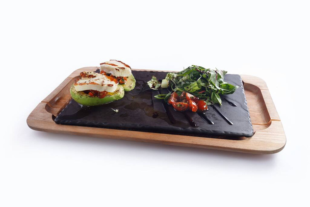 The sliced avocadoes with goat cheese next to tomatoes, beetroot leaves seasoned with olive oil on a wooden board - Foto, Bild
