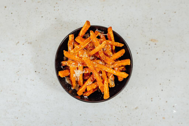 A closeup shot of a bowl of sweet potato fries on a white table - Фото, изображение