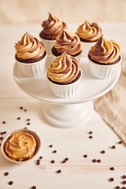 A vertical shallow focus closeup shot of delicious peanut butter cupcakes with a creamy icing in a white plate - Fotografie, Obrázek