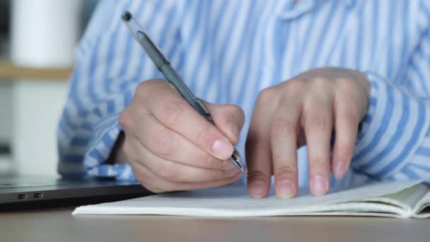 Ręka kobiety pisze zadania w notatniku siedzącym przy stole w kuchni w domu - Materiał filmowy, wideo