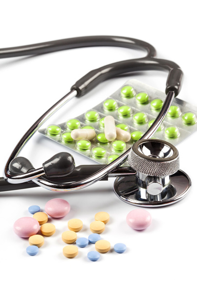 Multi color pills spills around the stethoscope, one blister with green pills, isolated on white - Photo, Image
