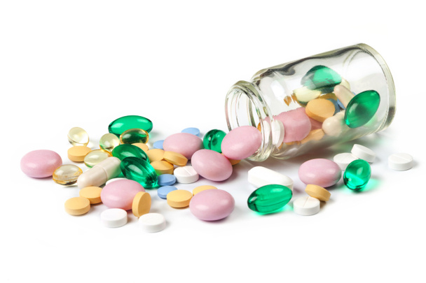 Multi kleur pillen morsen uit de kleine pot, fles, geïsoleerd op wit - Foto, afbeelding