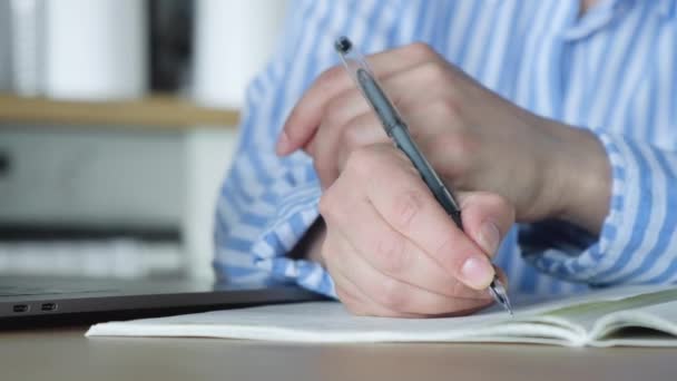 Primo piano della mano di una donna che tiene una penna e scrive note in un taccuino seduto a casa - Filmati, video