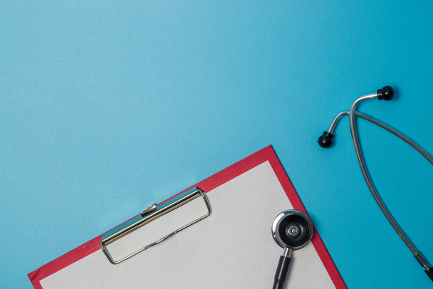 Stethoscope near paper in folder laying isolated on blue background - 写真・画像