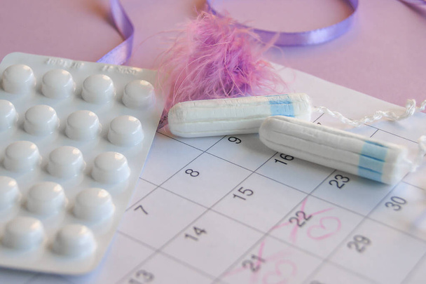 Menstruatie pads en tampons op menstruatie periode kalender met op lila achtergrond. - Foto, afbeelding