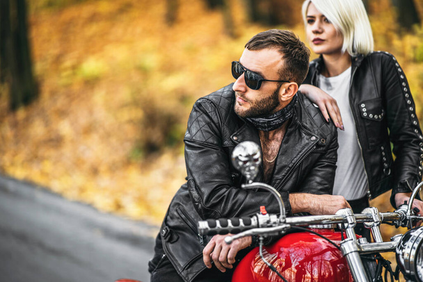 Pretty couple near red motorcycle on the road in the forest with colorful blured background. Relationship concept. - Fotografie, Obrázek