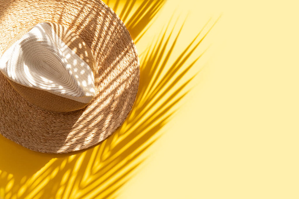 Sun protection object. Straw woman's beach hat and palm shadow on bright yellow backdrop. Beach accessory. Summer Travel Vacation Concept. Sale kit. Copy space. top view  - Foto, immagini