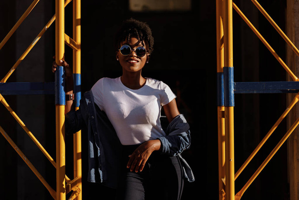 fille noire près du chantier de construction dans la ville en plein soleil - Photo, image