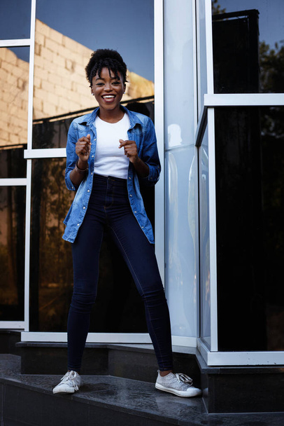 Black girl dances on a blue background outside the building - Photo, Image