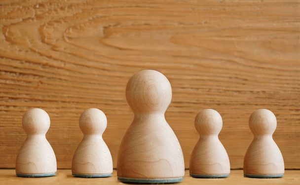 five 5 wooden figure persons with same brown or yellow color on wooden background. family sign, symbol. one big boss in the middle. - Photo, image