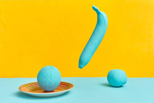 painted banana orange apple in turquoise color on a yellow background. creativity design concept - Фото, изображение