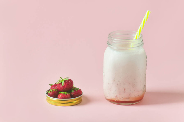 milk strawberry smoothie on pink background. handful of ripe strawberries in a jar lid - Фото, изображение