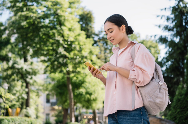Beautiful asian woman using smartphone, shopping online, communication, checking email, walking in park. Mobile banking concept - Fotografie, Obrázek
