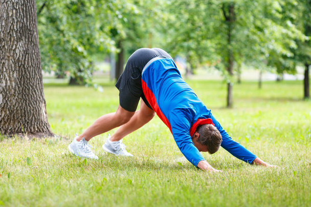 Man practice yoga in park. Adult man do downward facing dog pose. - Photo, Image