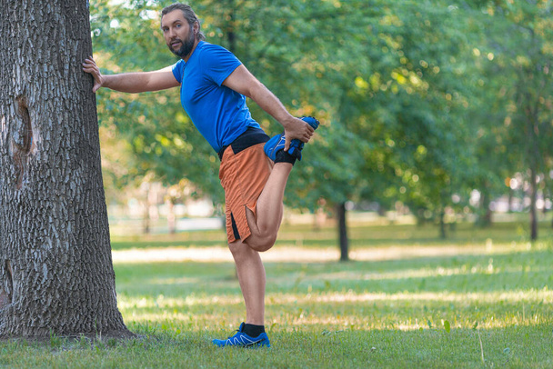 Man warming up muscles before jogging outdoor in summer time. - Photo, Image