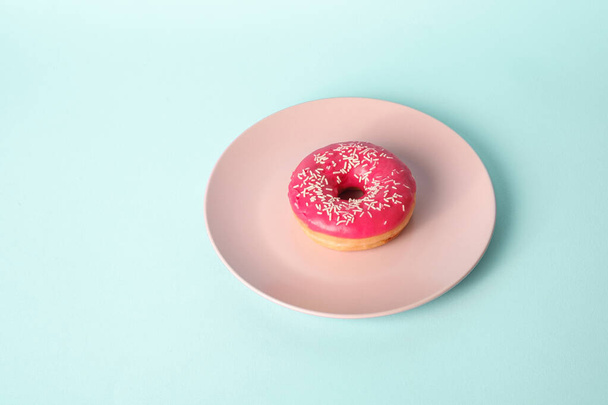 rosa roter Donut mit weißen Streusel auf rosa Teller, süß glasierte Dessertspeise auf blauem Hintergrund, Winkelansicht - Foto, Bild