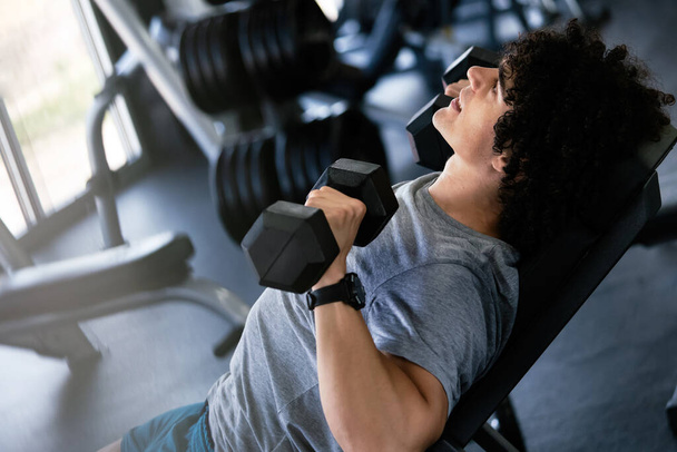 Muscular fit man working out in gym doing exercises with dumbbells at biceps - Foto, imagen