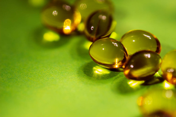 Kapsüllerdeki vitaminler yeşil zemin üzerinde sarıdır. Yakın plan. Vücut sağlığı için vitamin ve mineral eksikliği kavramı.. - Fotoğraf, Görsel