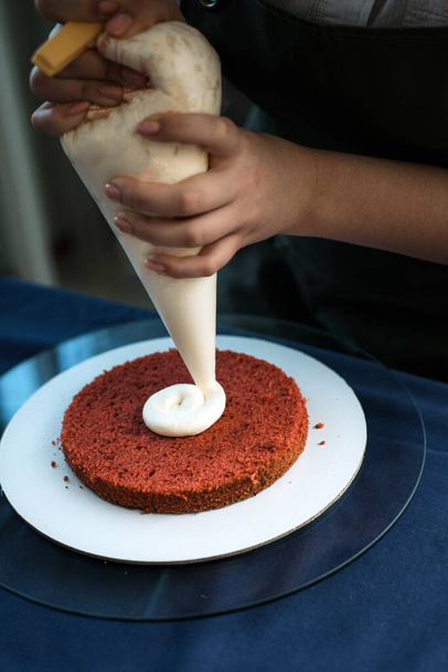 Las manos de una chica panadera aprietan crema rosa sobre una base de pastel - Foto, Imagen