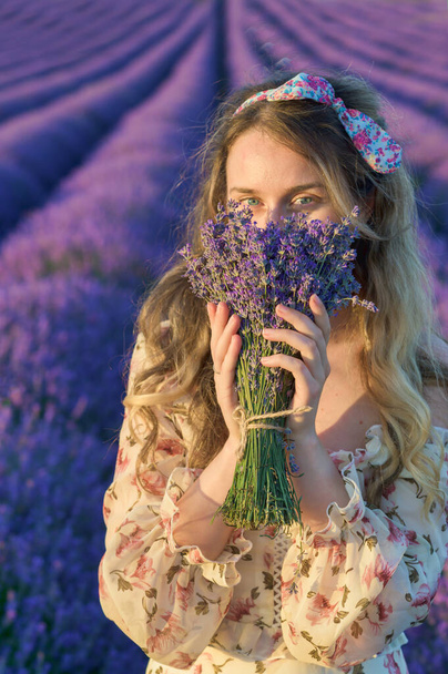 Woman smelling a lavender bouquet. Happy dreamy smile. Cute summer dress curly hair - Valokuva, kuva