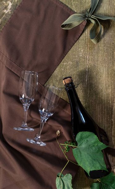 Wijnfles en glazen op de houten ondergrond met bruin schort. Concept van bezorgservice voor de klant. - Foto, afbeelding